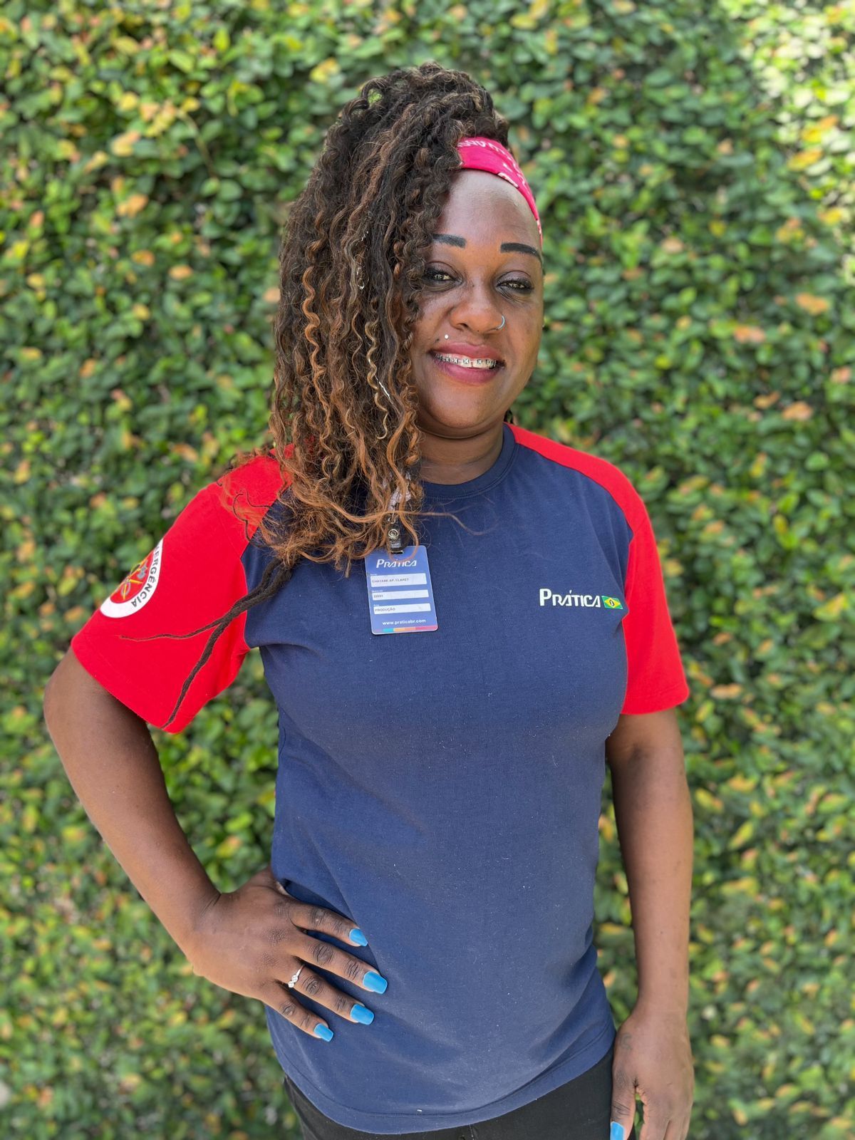 Uma mulher vestindo uma camisa azul e vermelha está parada em frente a uma parede verde.