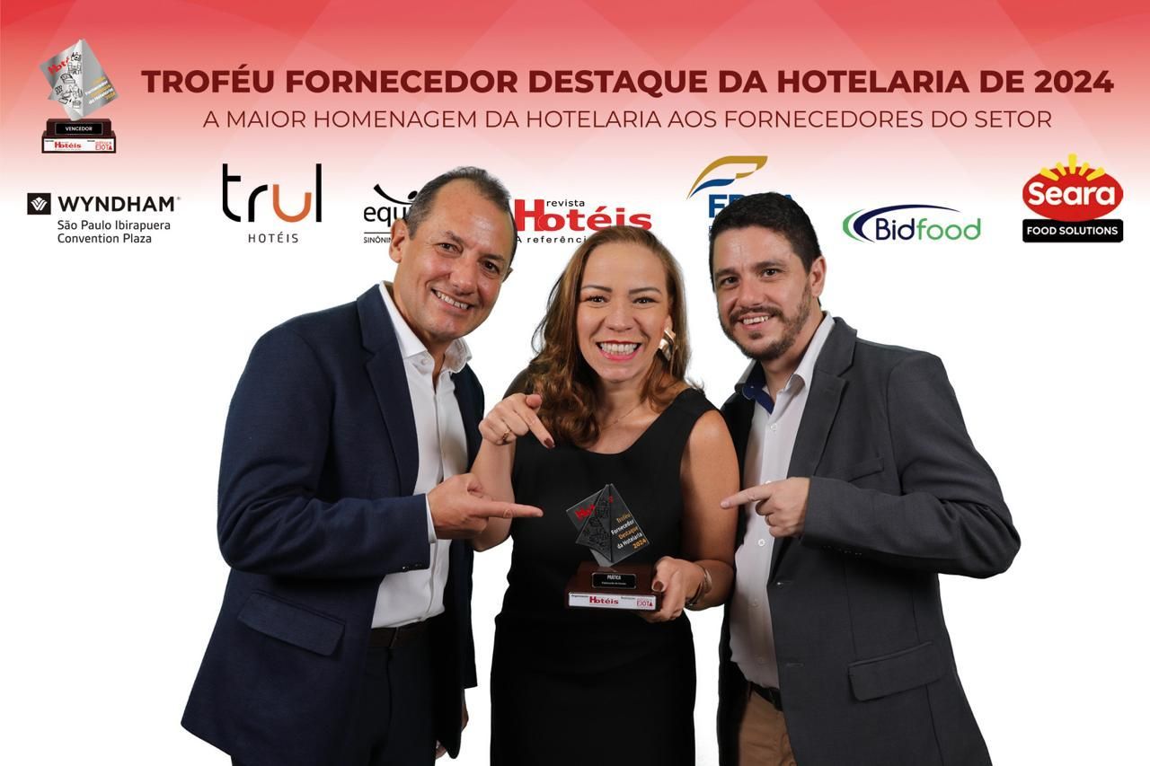 Três pessoas posam para foto em frente a uma placa que diz troféu fornecedor destaque da hotelaria de 2024
