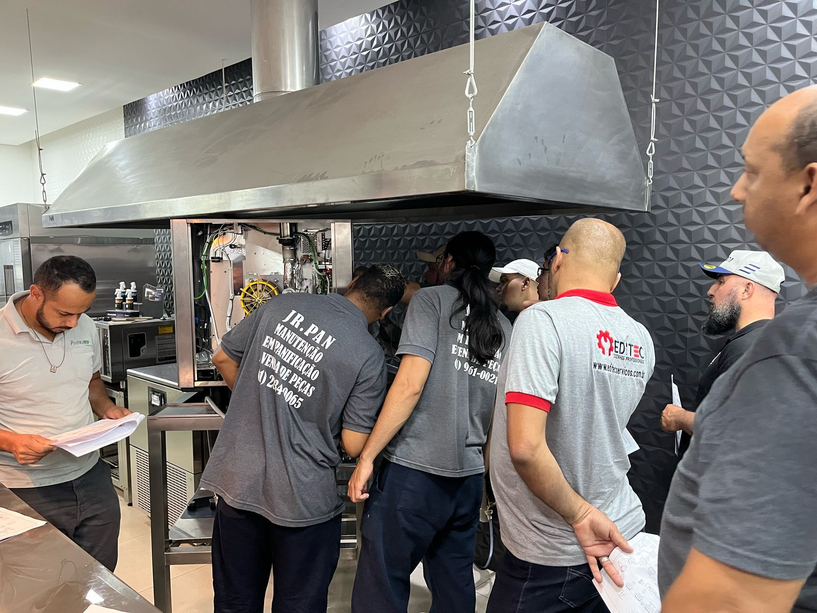 Um grupo de homens está em uma cozinha olhando papéis.