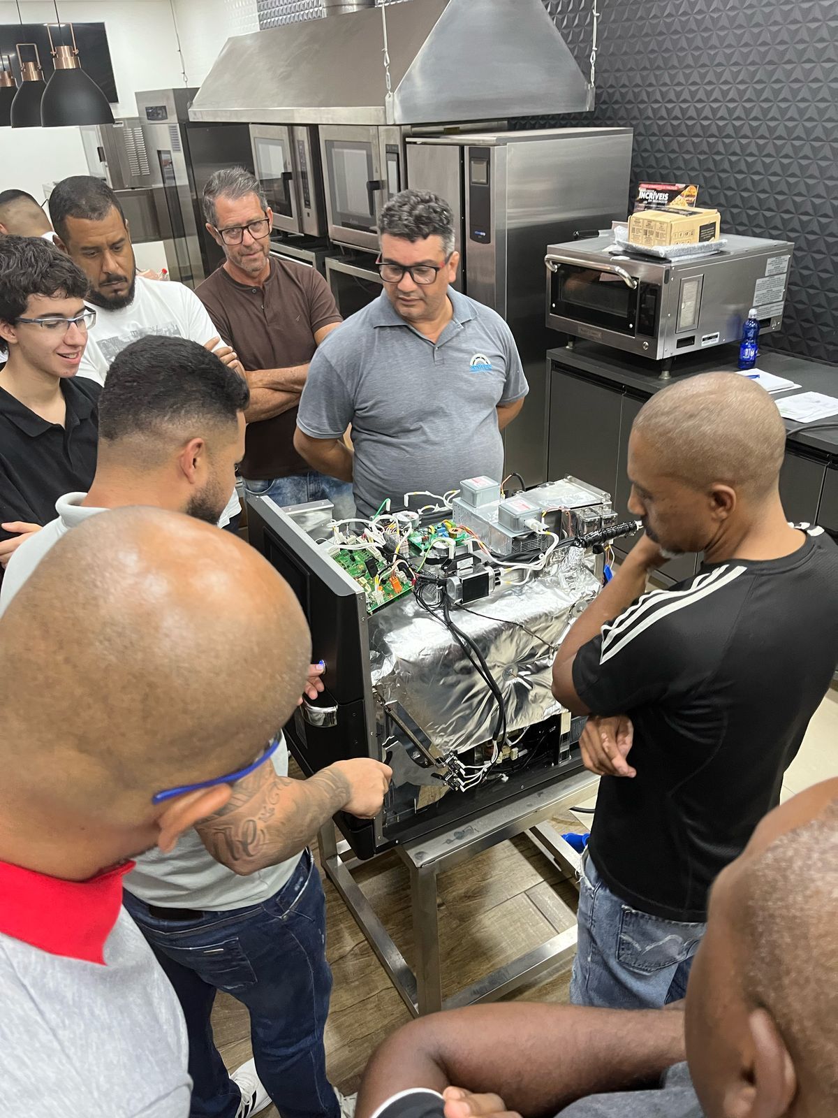 Um grupo de homens está em volta de uma máquina em uma cozinha.