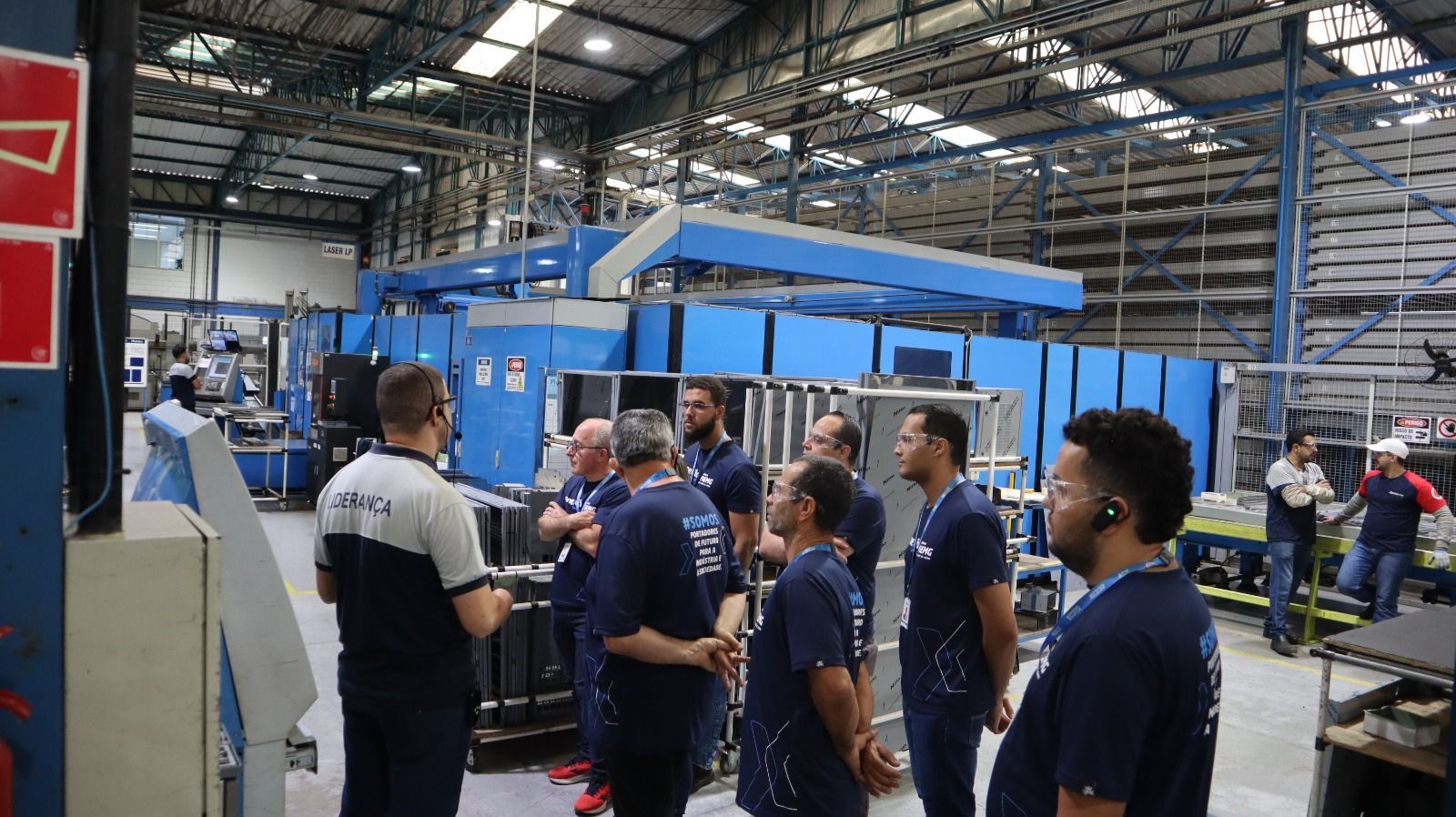 Um grupo de homens está em uma fábrica conversando entre si.