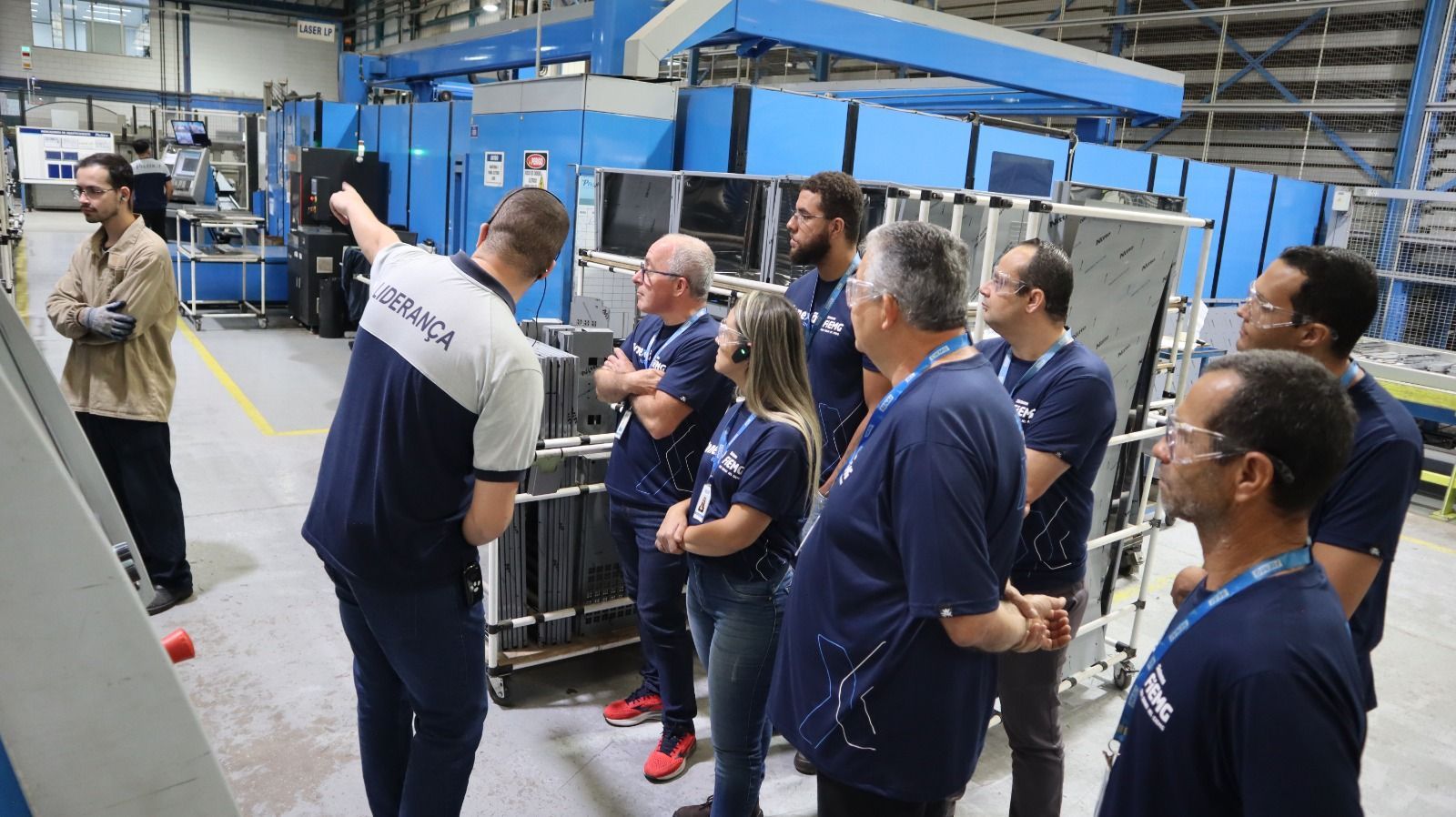 Um grupo de pessoas está em uma fábrica olhando para uma máquina.
