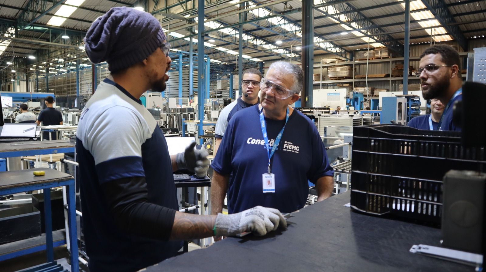 Um grupo de homens está em uma fábrica conversando entre si.