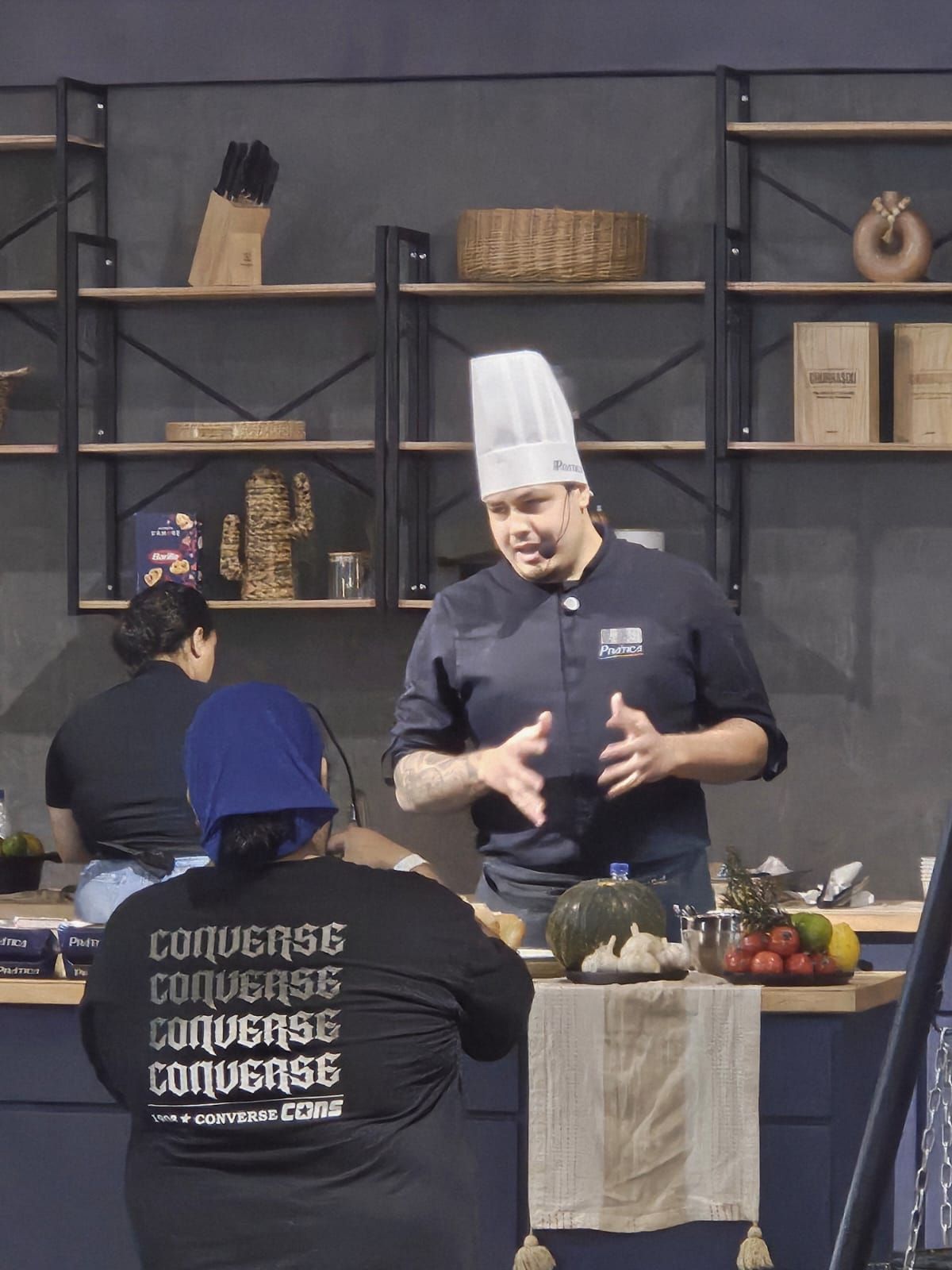 Um homem com um chapéu de chef está conversando com uma mulher com uma camisa preta que diz converse nas costas.