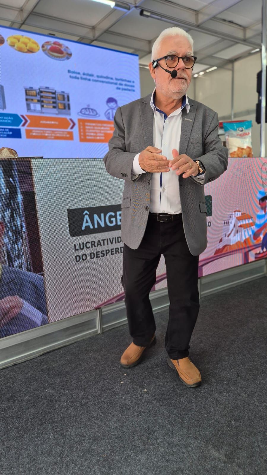 Um homem de terno e óculos está parado em frente a uma tela grande.