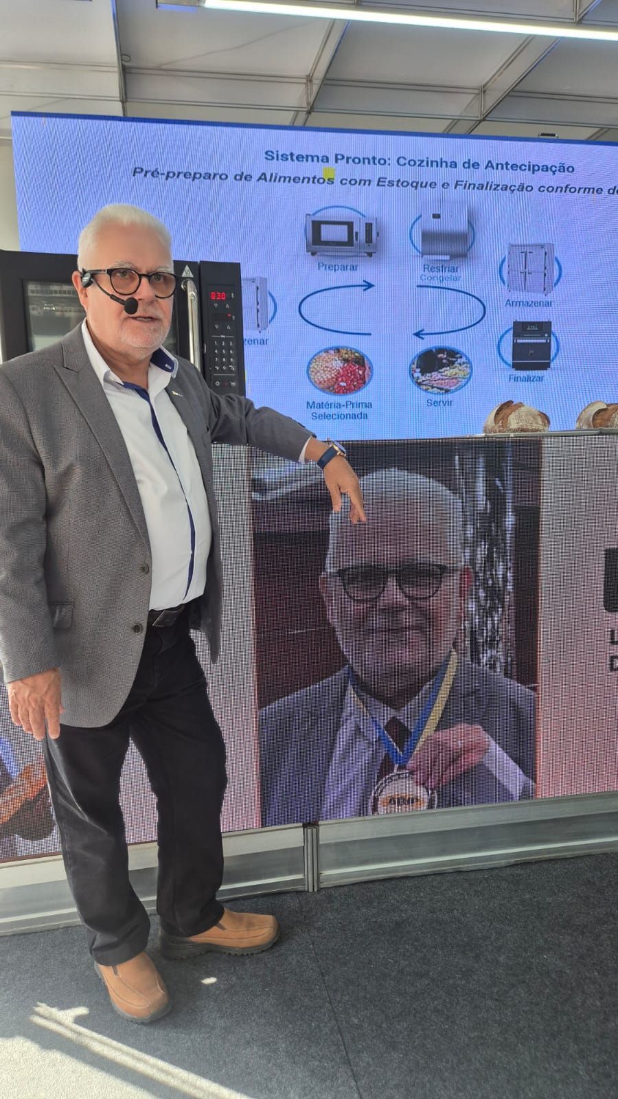 Um homem de terno e gravata está parado em frente a uma tela grande.