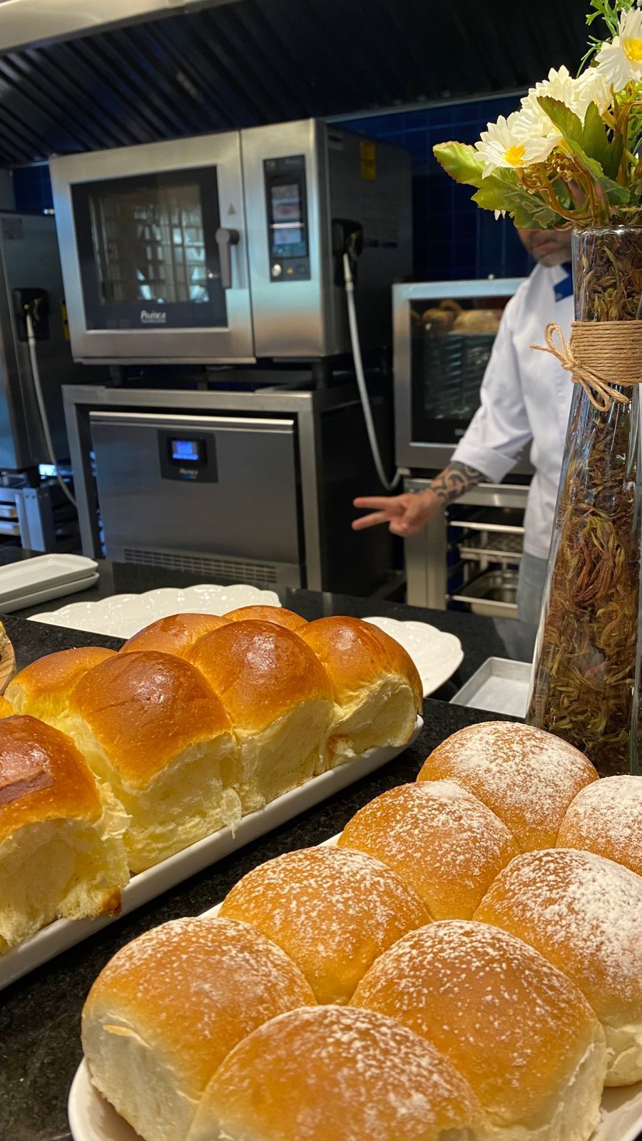 Um chef está em pé na cozinha ao lado de um monte de pãezinhos.
