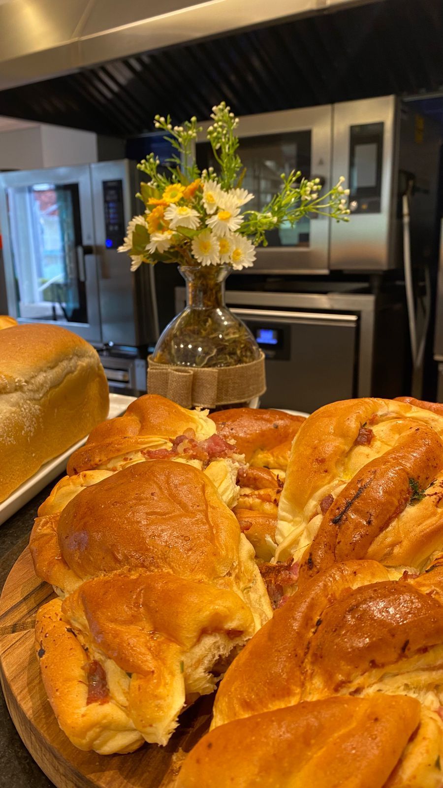 Um monte de pão e um vaso de flores sobre uma mesa na cozinha.