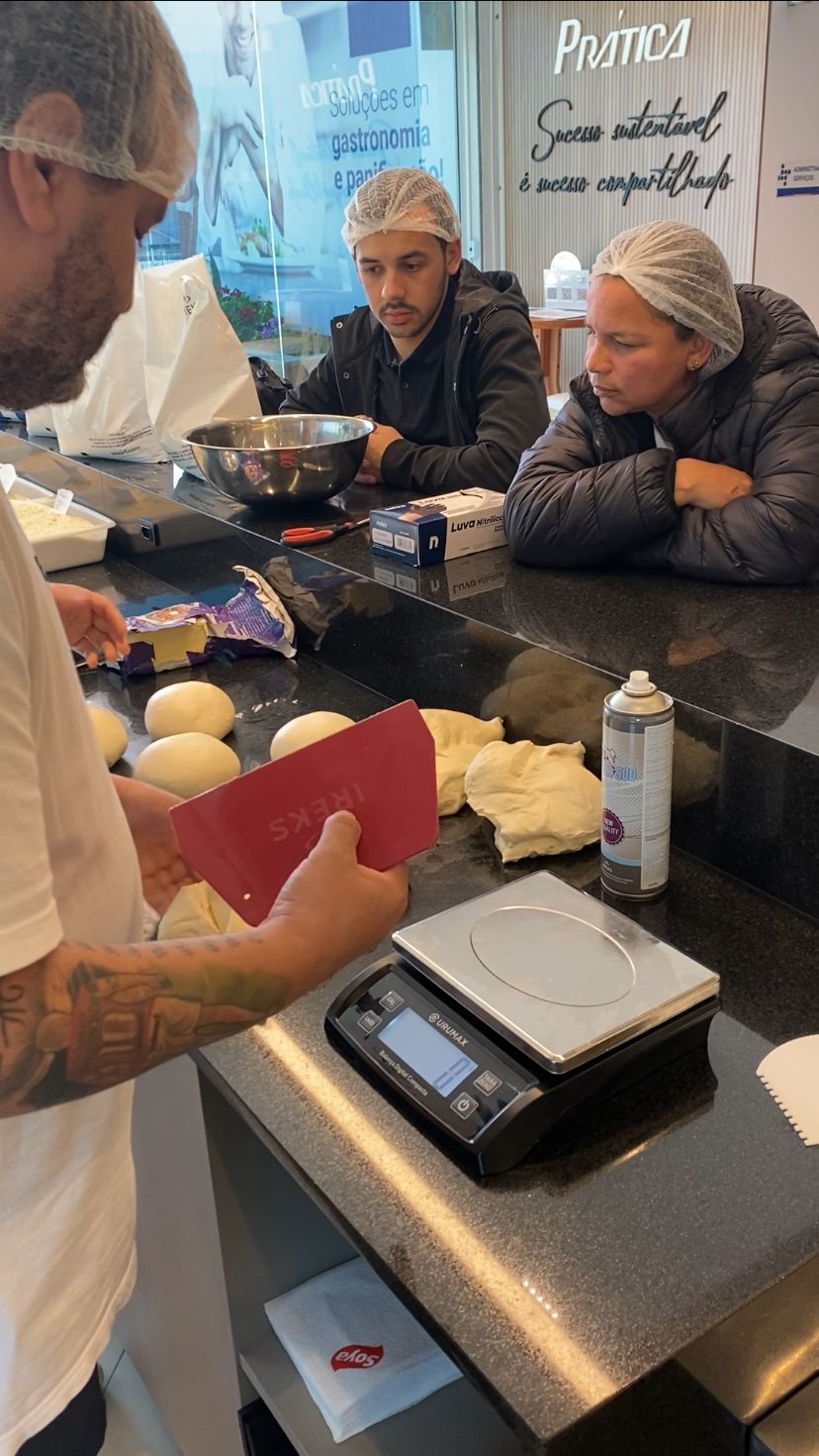 Um homem segura um pedaço de massa ao lado de uma balança em uma cozinha.