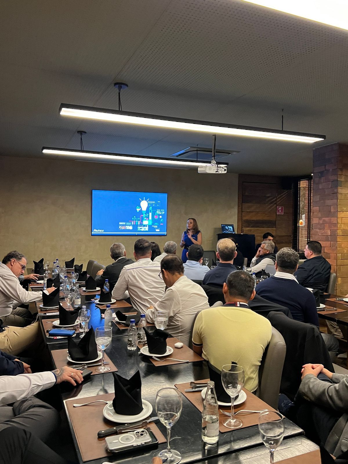 Uma mulher está fazendo uma apresentação para um grupo de pessoas sentadas em mesas.