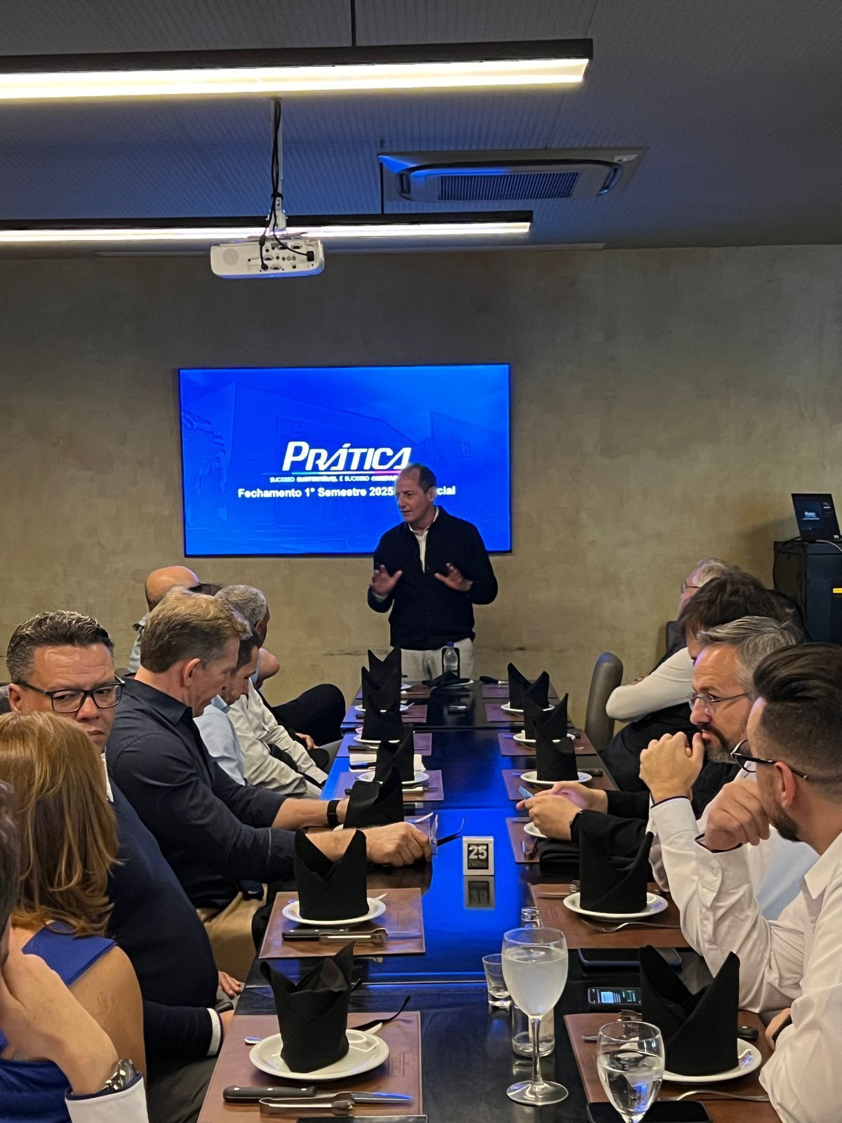Um homem está fazendo uma apresentação para um grupo de pessoas sentadas ao redor de uma mesa.