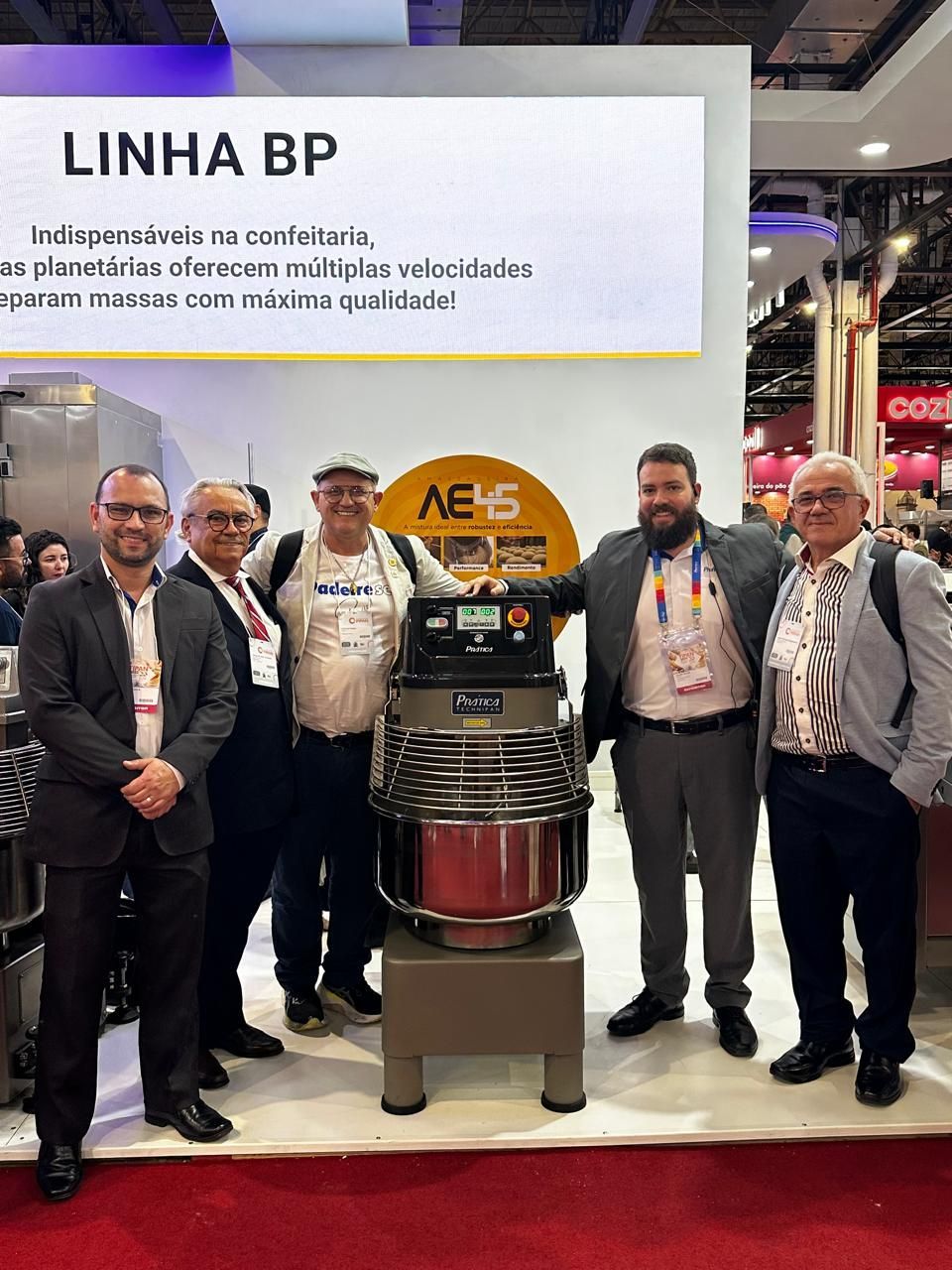 Uma multidão de pessoas reunidas ao redor de um estande em uma feira comercial.