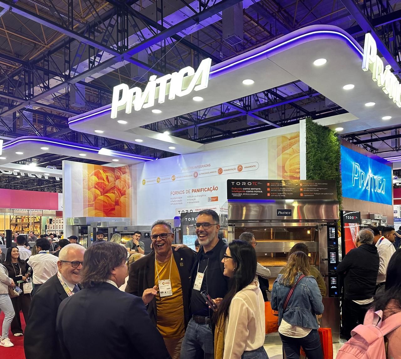 Um grupo de pessoas está sentado ao redor de uma mesa conversando com um homem com chapéu de chef.