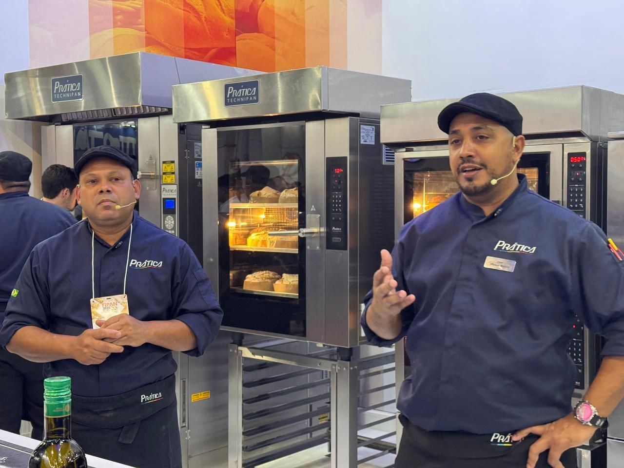 Dois homens estão em pé em frente a um forno conversando entre si.