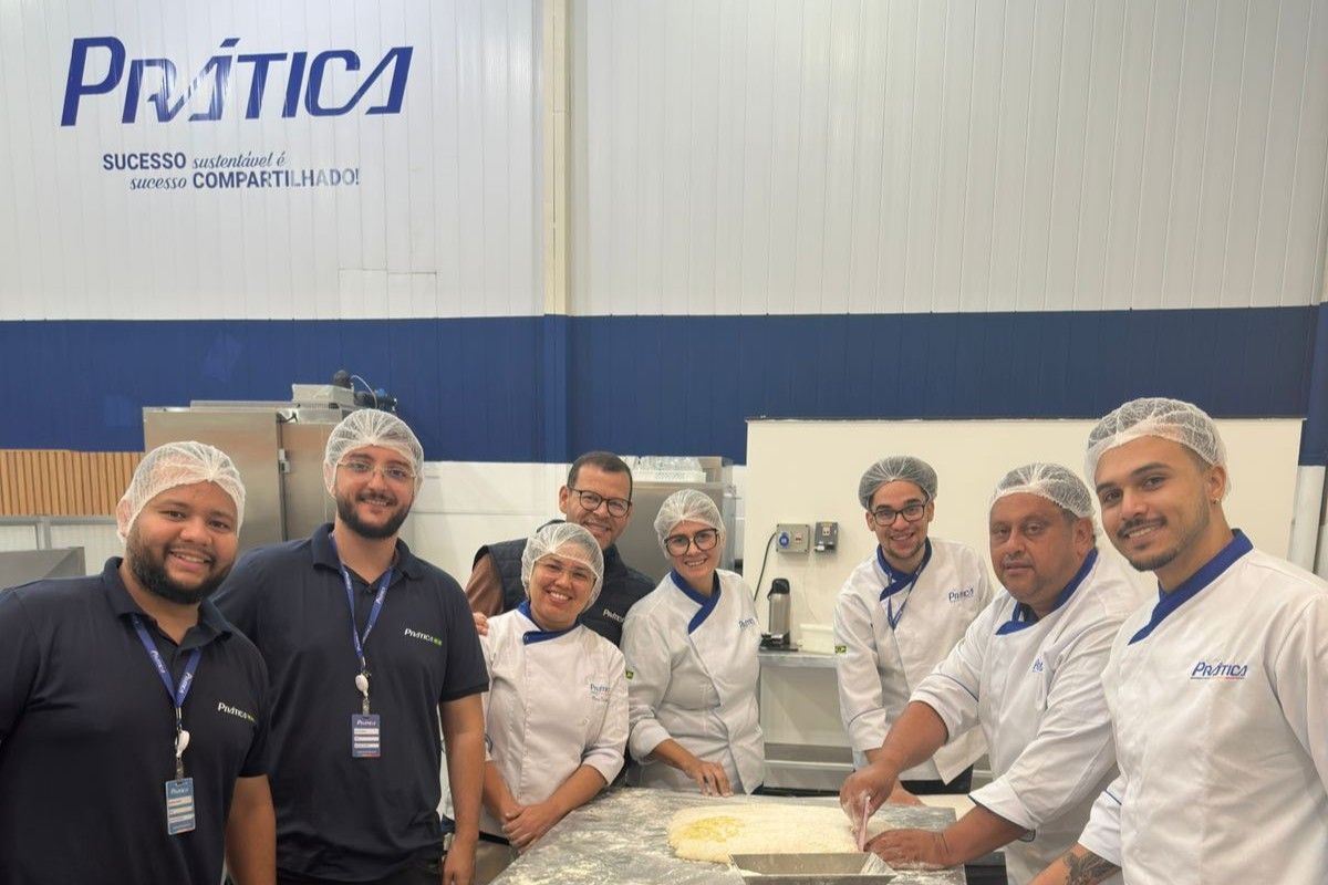 Grupo de padeiros de jaleco branco e touca de cabelo perto de um balcão. Logotipo da