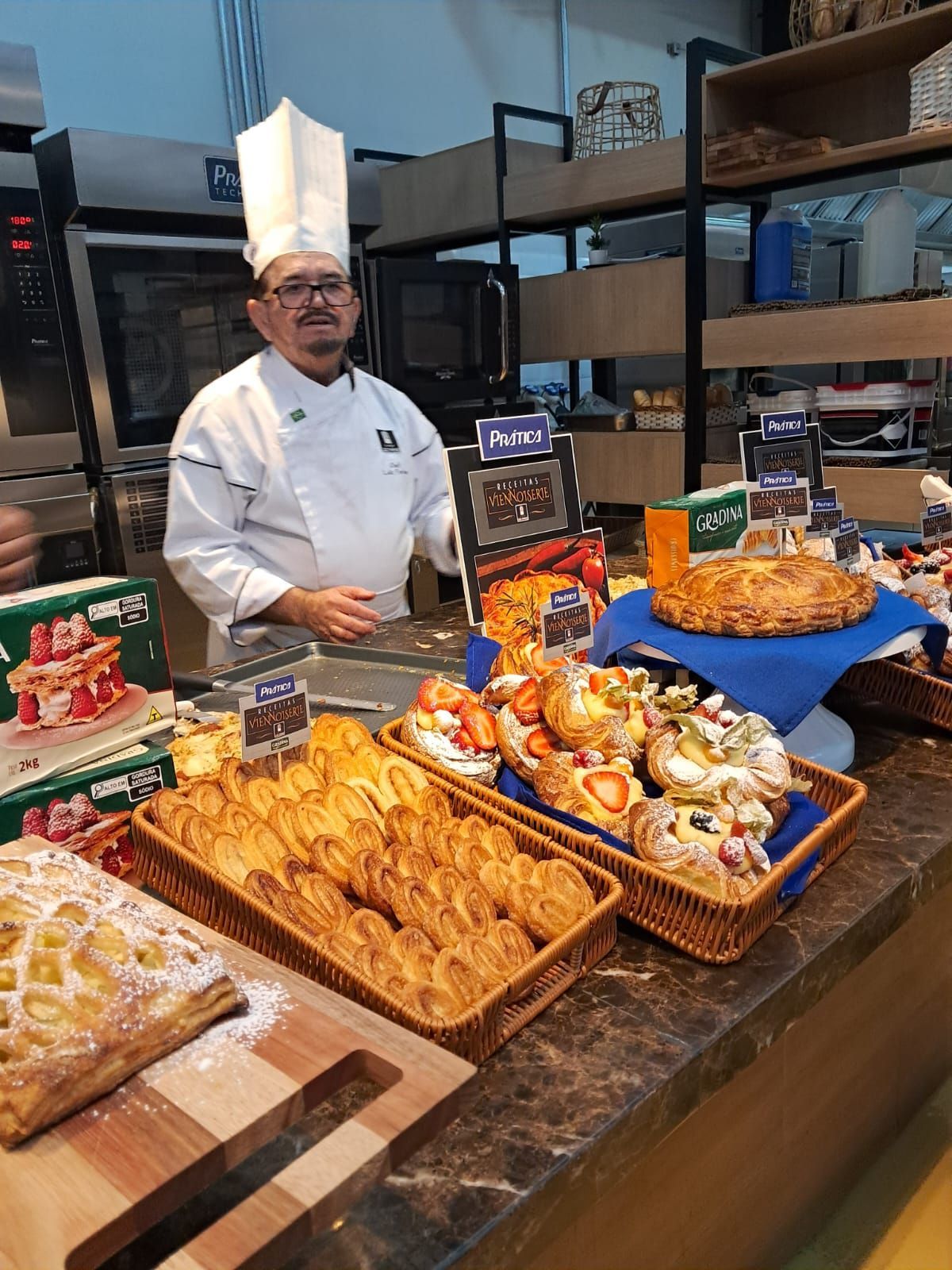 Chef de uniforme branco e chapéu fica atrás de um balcão de doces.