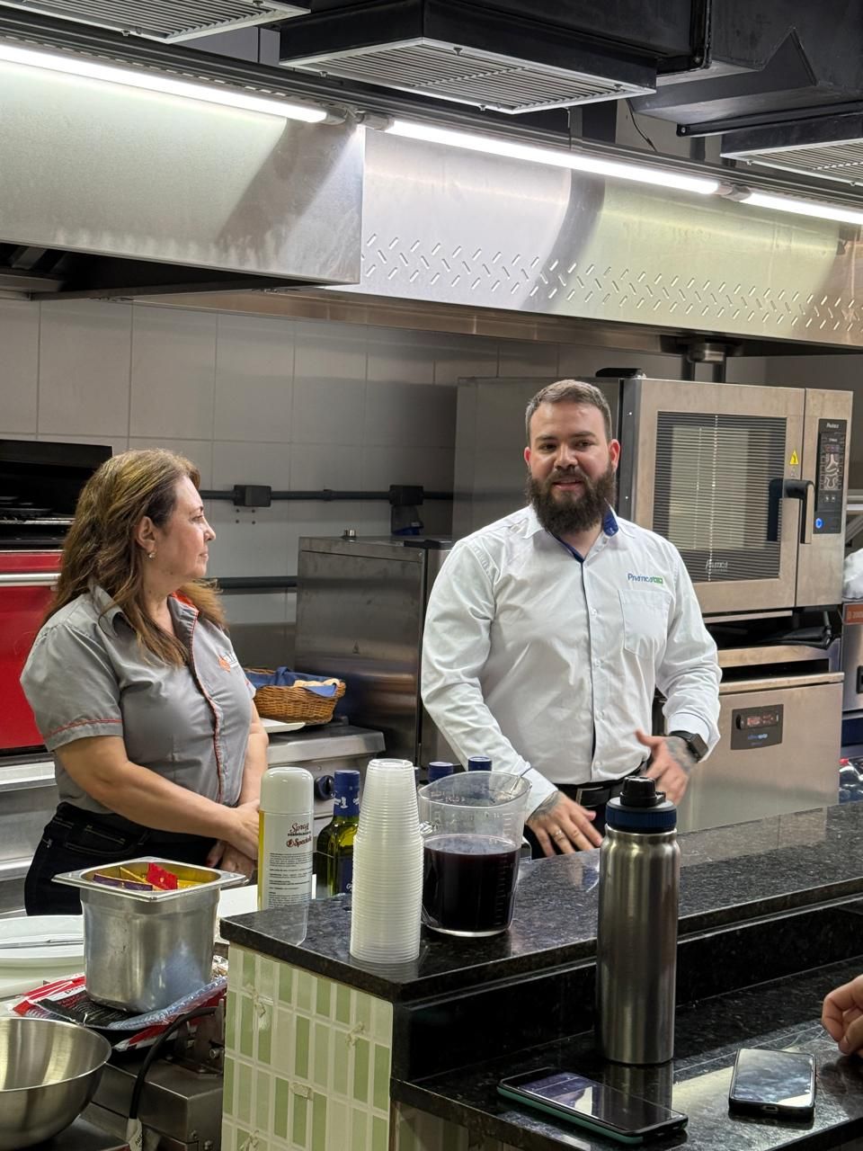 Homem e mulher em uma cozinha, o homem falando, a mulher ouvindo. Cozinha com eletrodomésticos e balcão de aço inoxidável.
