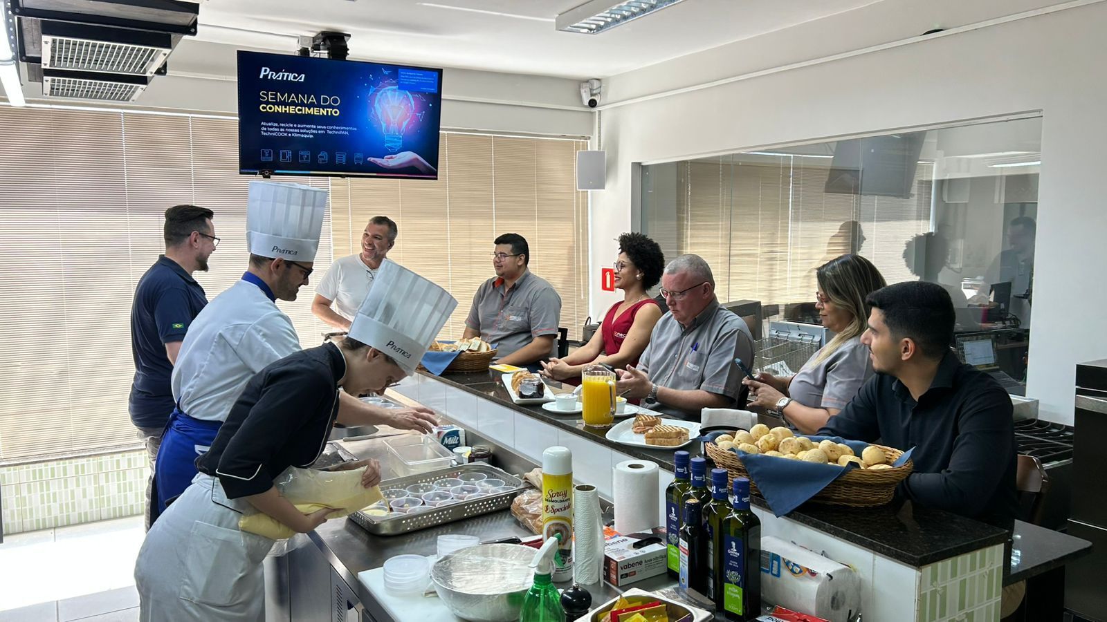 Chefs preparando comida atrás de um balcão com um grupo de pessoas sentadas em um bar, observando-os.