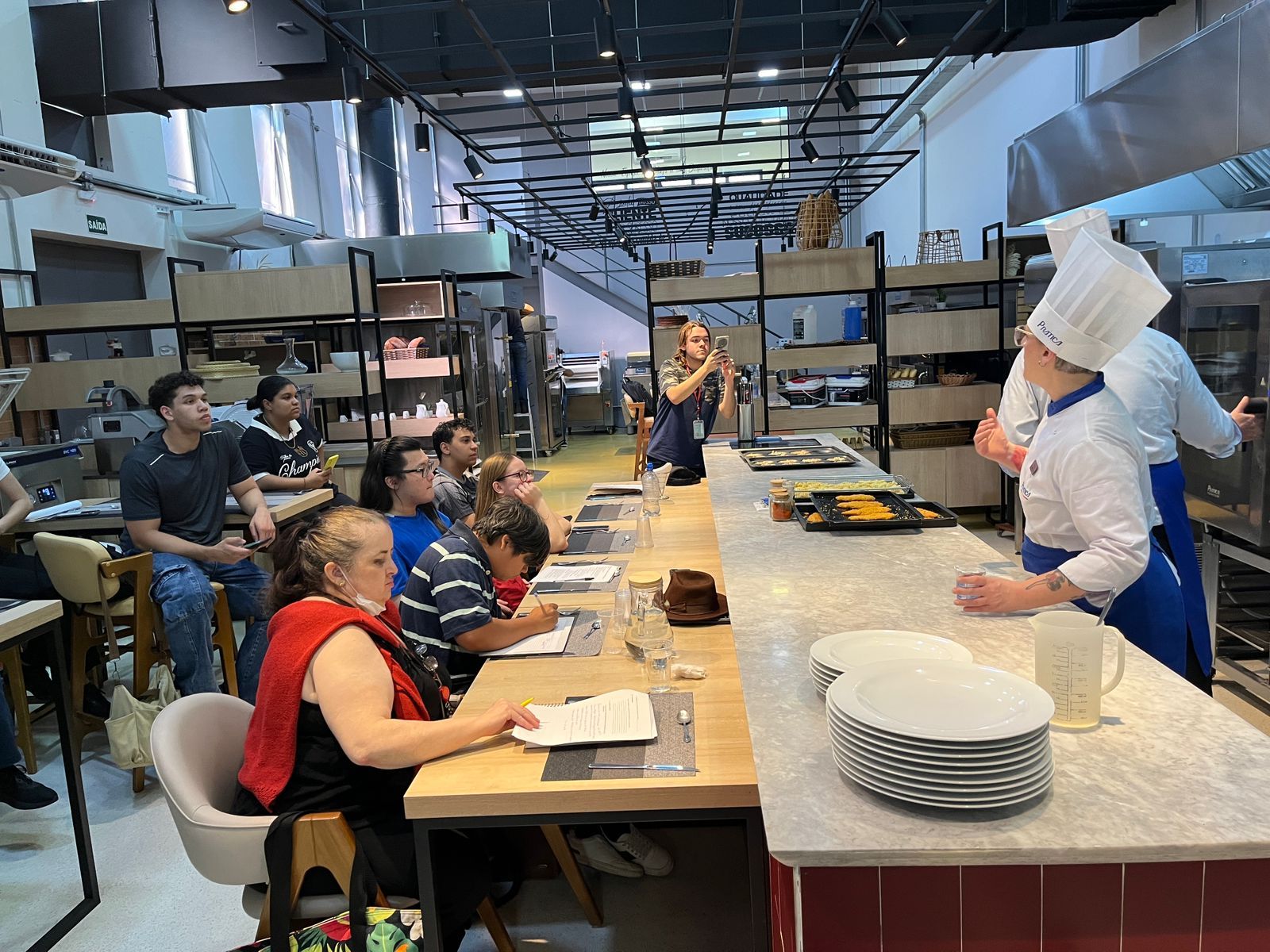 Um chef demonstra culinária para um grupo em uma cozinha profissional.