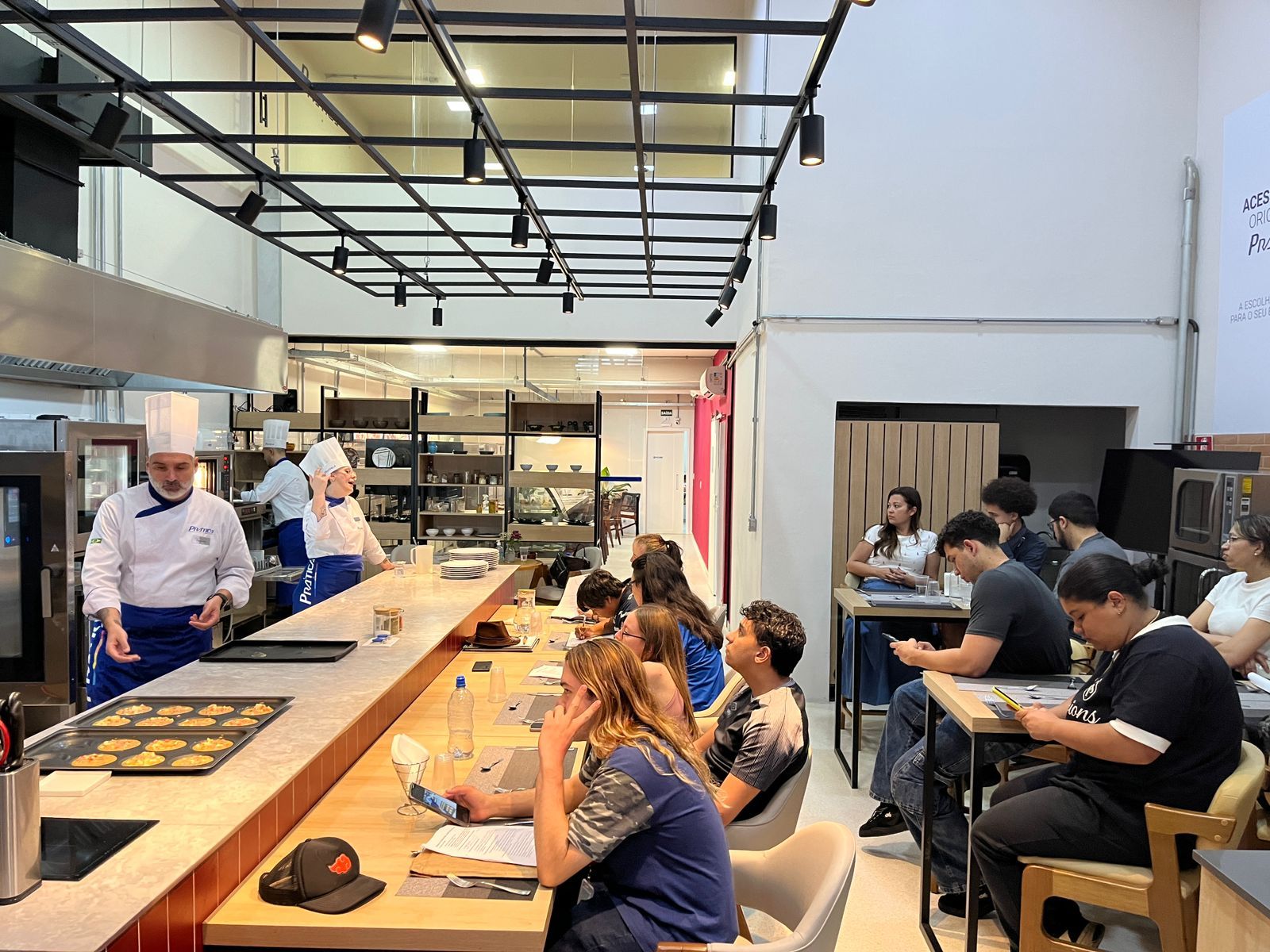 Chef dando uma demonstração de culinária para um grupo de estudantes em uma cozinha profissional.