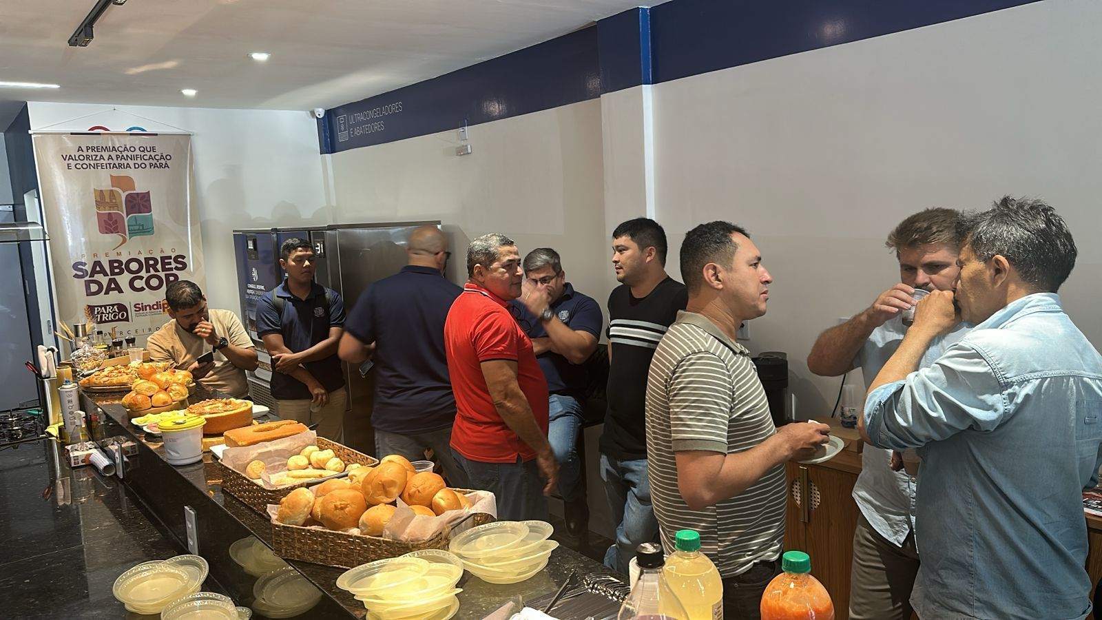 Pessoas se reuniam em um balcão, provavelmente uma padaria, olhando e comendo comida.