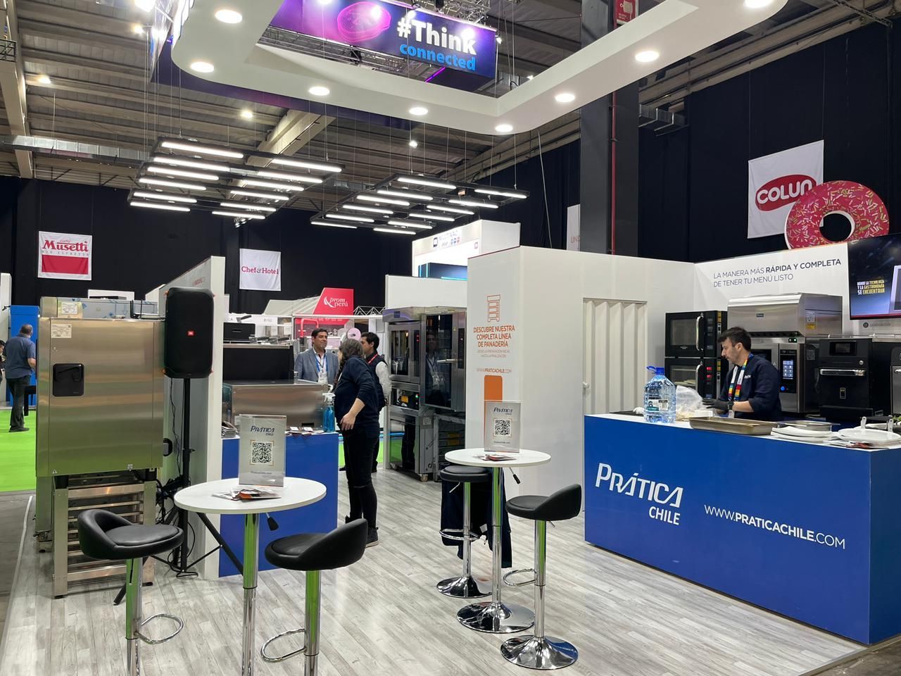 Estande de feira com máquinas, pessoas e sinalização promocional.