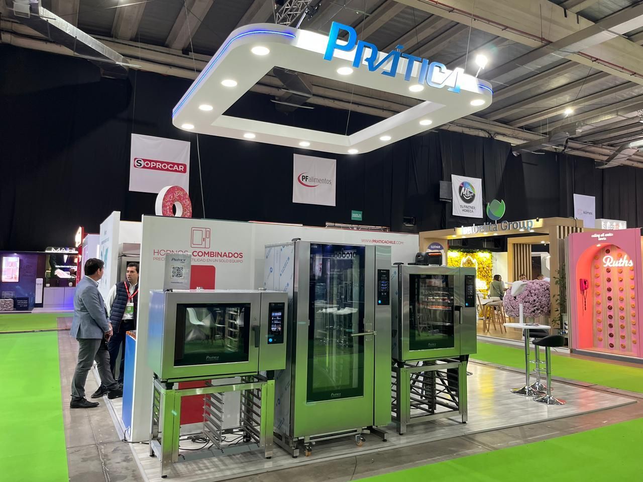 Estande em uma feira comercial, apresentando fornos comerciais. Pessoas em pé perto dos fornos sob uma placa