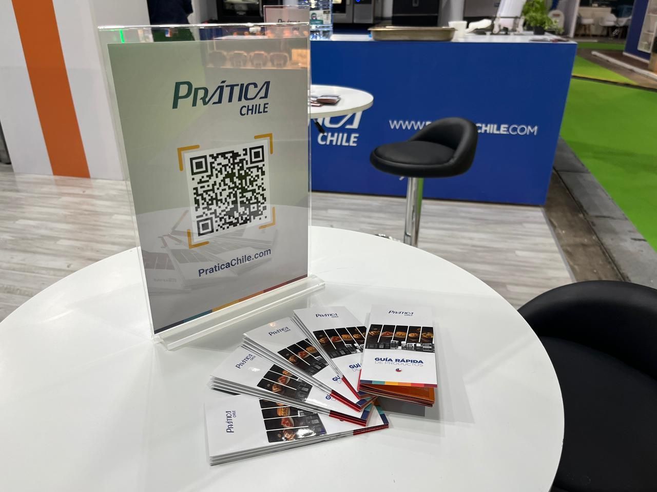 Uma mesa com um display de código QR, folhetos e um banco em uma feira comercial.