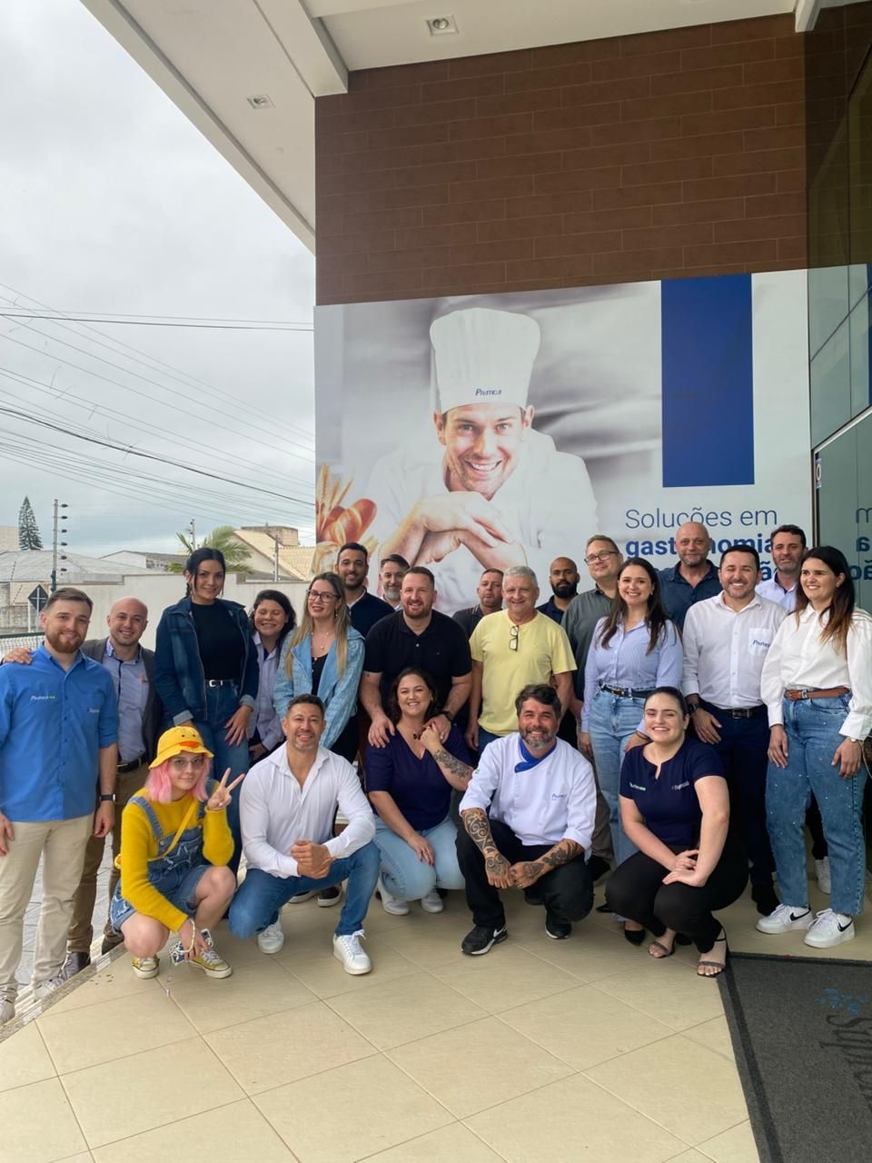 Grupo de pessoas posando do lado de fora de um prédio, com um grande mural de chef.