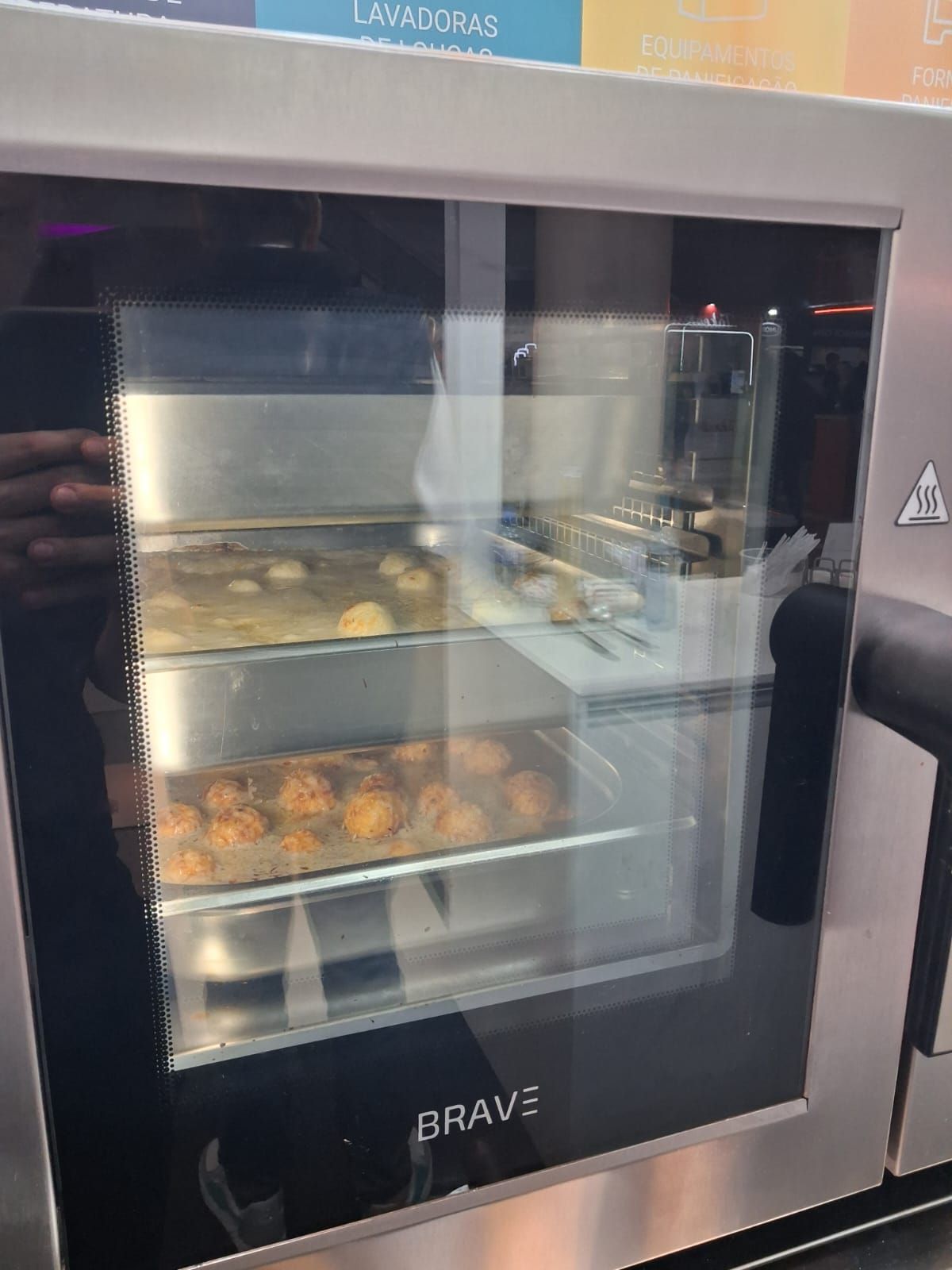 Um forno comercial com três prateleiras de alimentos dentro, visto através da porta de vidro. 