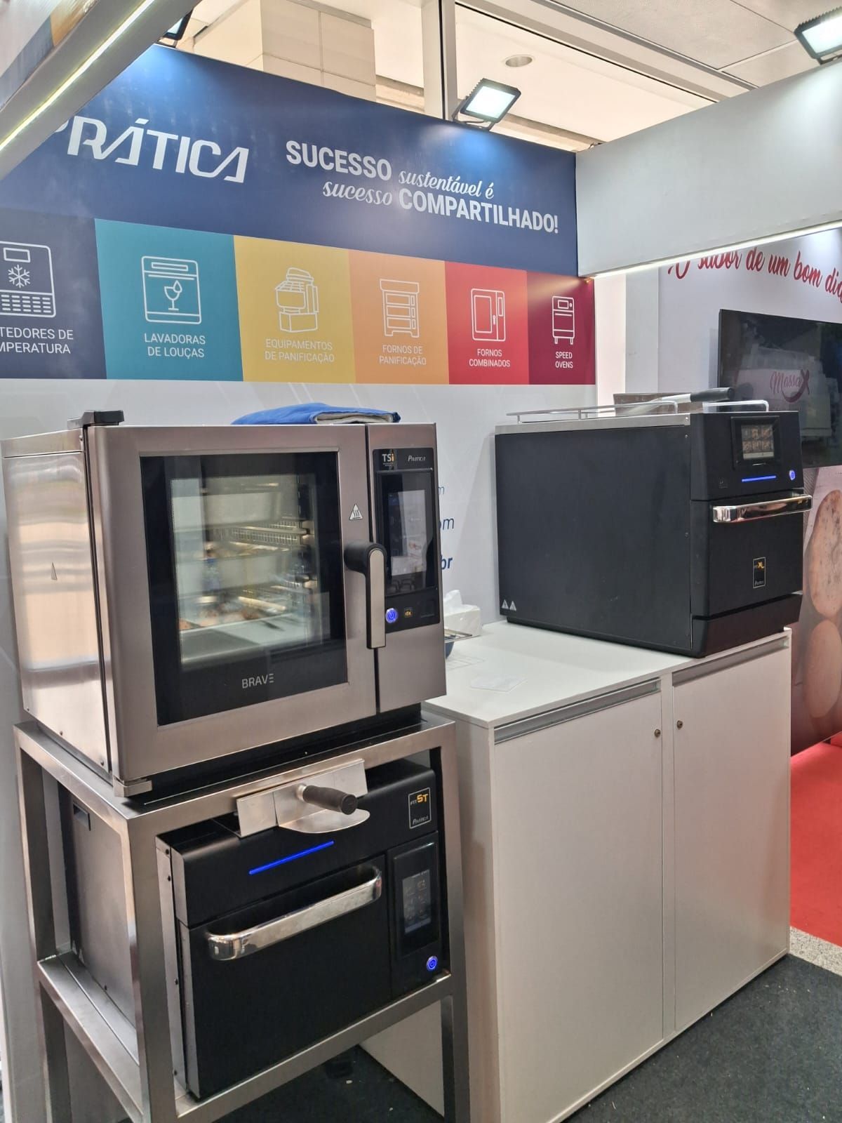 Fornos comerciais em uma feira. Modelos em aço inoxidável e pretos expostos em estandes, com letreiros coloridos.