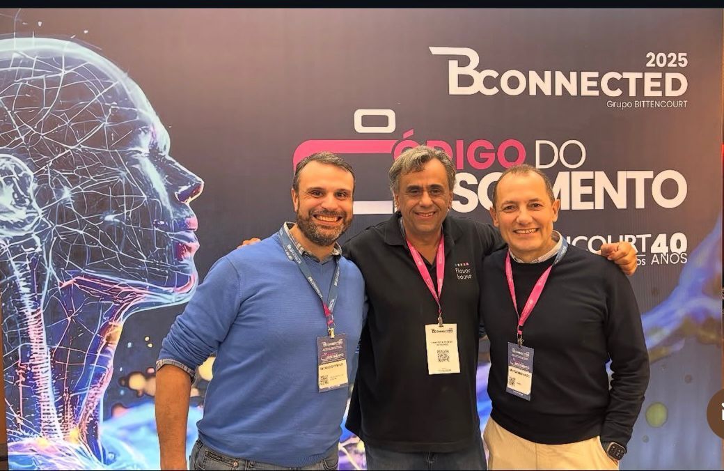 Três homens sorrindo, posando para foto em uma conferência com tema de tecnologia.