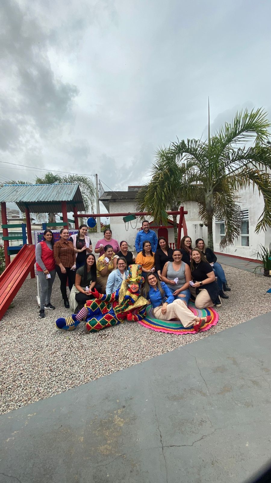 Grupo de pessoas posando ao ar livre; playground, dia nublado. Alguns estão ajoelhados, outros sentados, outros em pé.