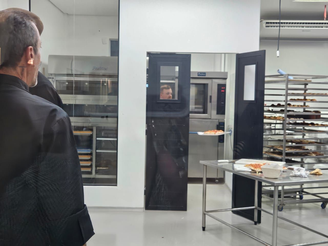 Homem de terno preto olhando para uma padaria com fornos e doces.