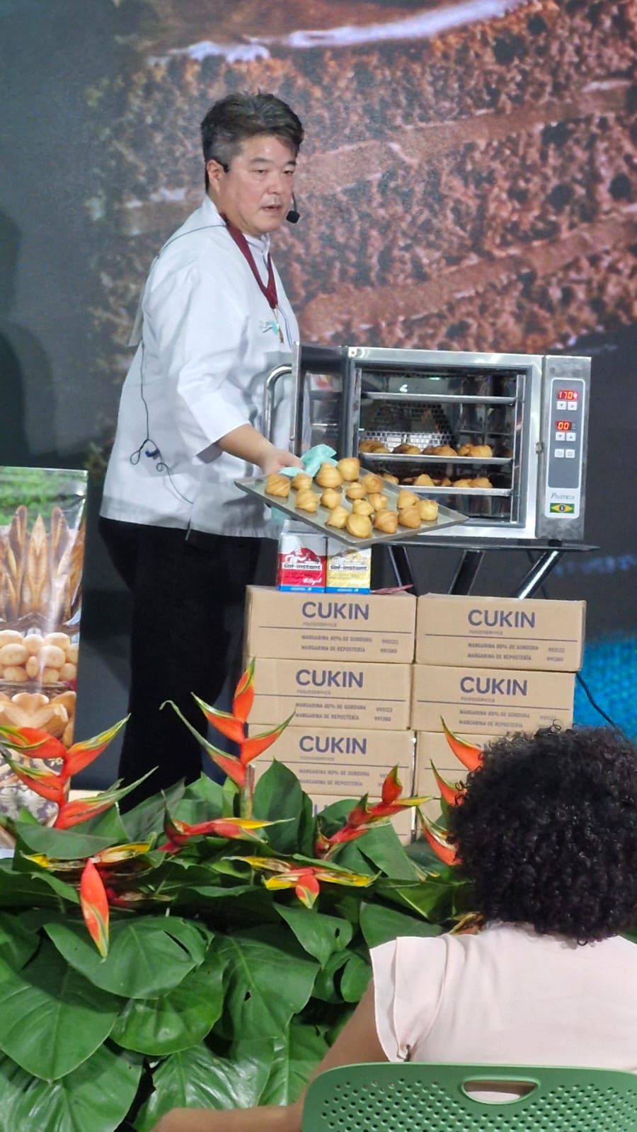 Chef segurando uma bandeja de produtos assados, retirando-os do forno durante uma apresentação.