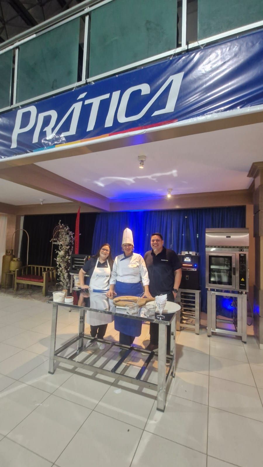 Três pessoas posam em frente a uma faixa 