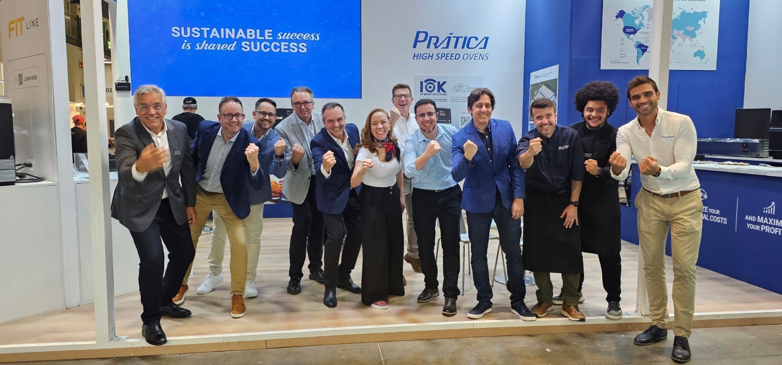 Grupo de pessoas em uma feira comercial, socando o ar em comemoração; fundo azul e branco.