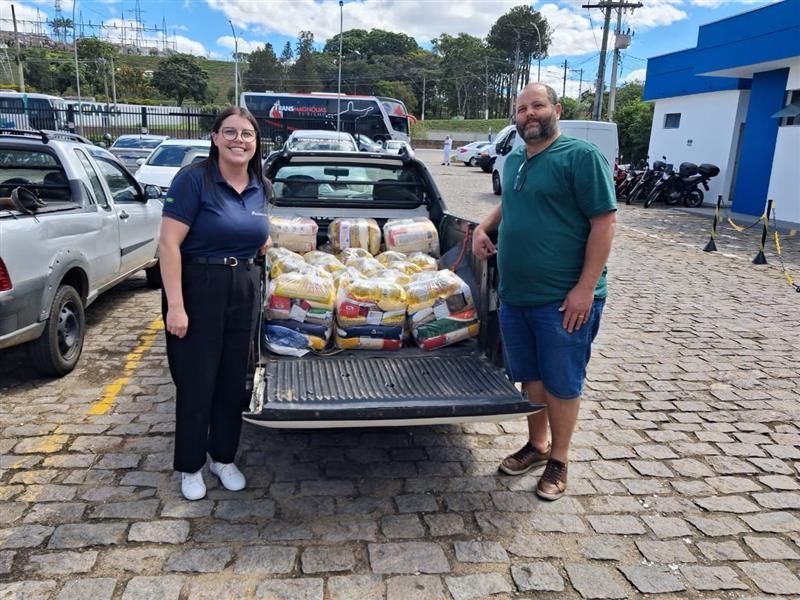 Duas pessoas estão perto de uma caminhonete carregada de sacos de comida. Elas sorriem em um ambiente externo.