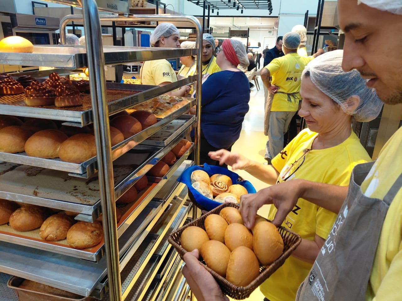 Pessoas em uma padaria, usando toucas e aventais, preparando e manuseando pão.