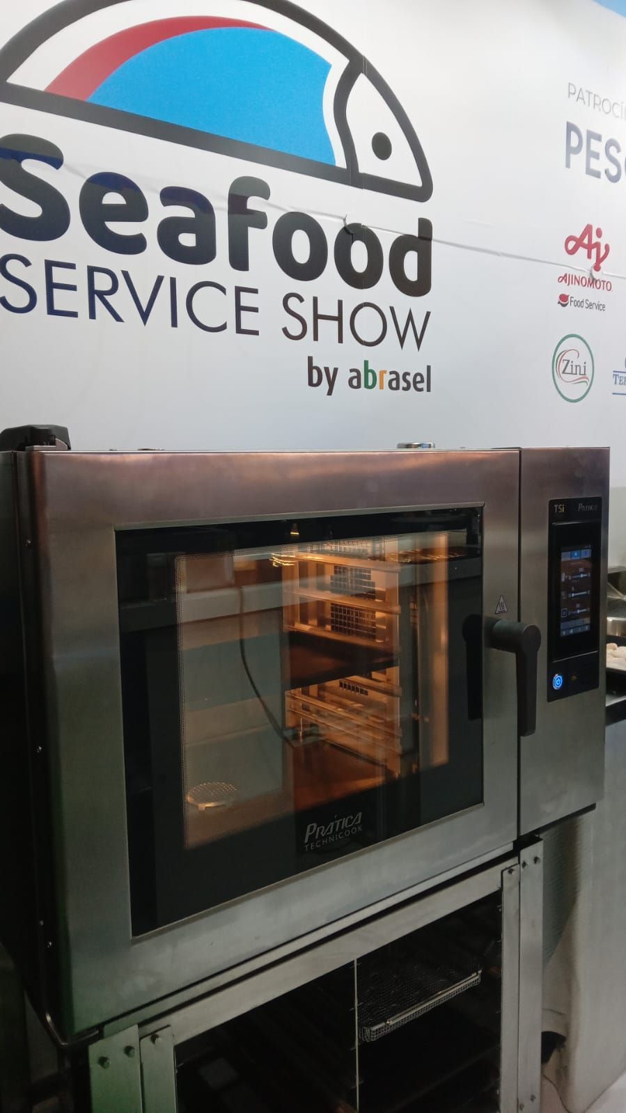 Forno comercial na Feira de Serviços de Frutos do Mar. Aço inoxidável, porta de vidro, alimentos dentro.