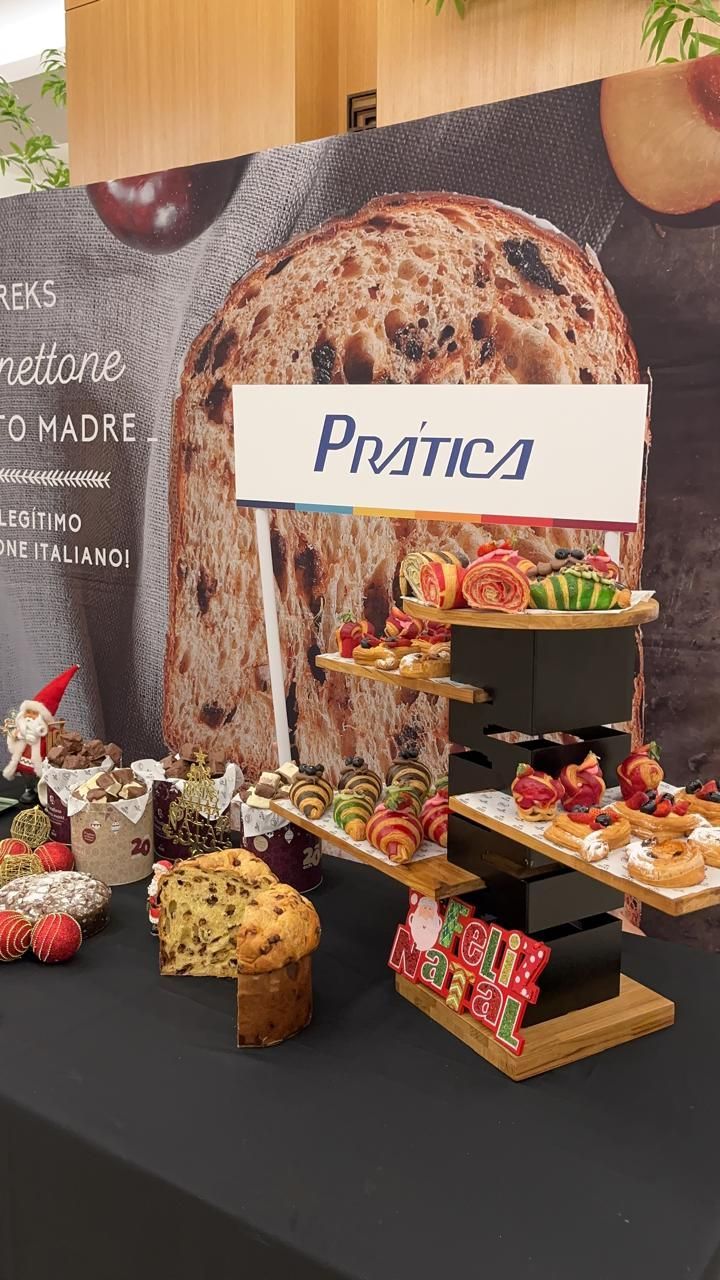 Exposição de produtos assados sobre uma toalha de mesa preta; placa com os dizeres
