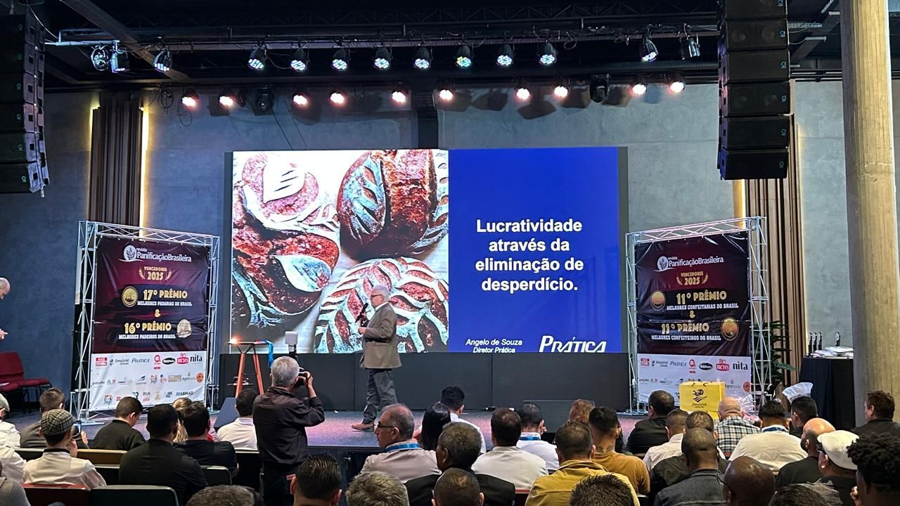 Palestrante no palco apresentando-se para uma plateia; um telão exibe texto e uma imagem de tecido cerebral.