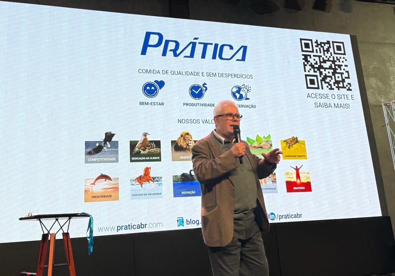 Homem discursando em uma conferência. A tela exibe o logotipo e ilustrações da