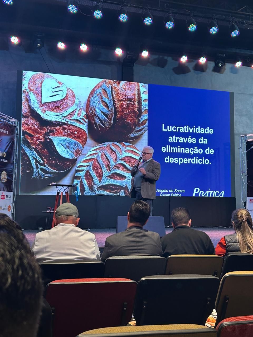 Homem fazendo uma apresentação sobre lucratividade através da eliminação de desperdícios, com imagens de pão na tela.