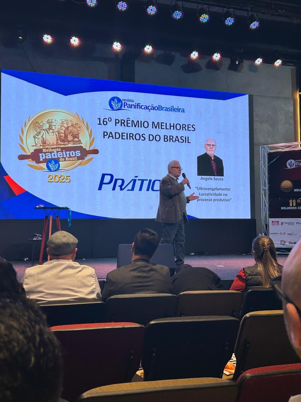 Man speaking at a podium; screen says