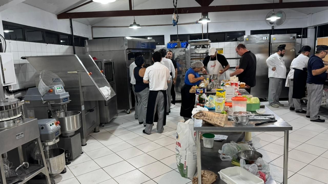 Cozinha comercial movimentada com pessoas trabalhando; eletrodomésticos e mesas de aço inoxidável.
