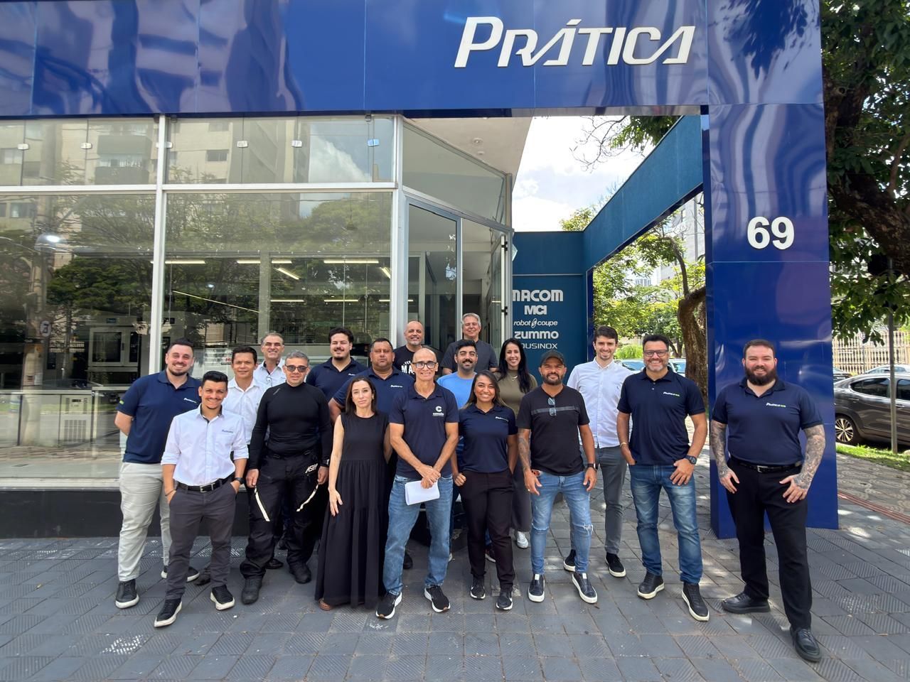Grupo de pessoas posando em frente a um prédio azul com o nome