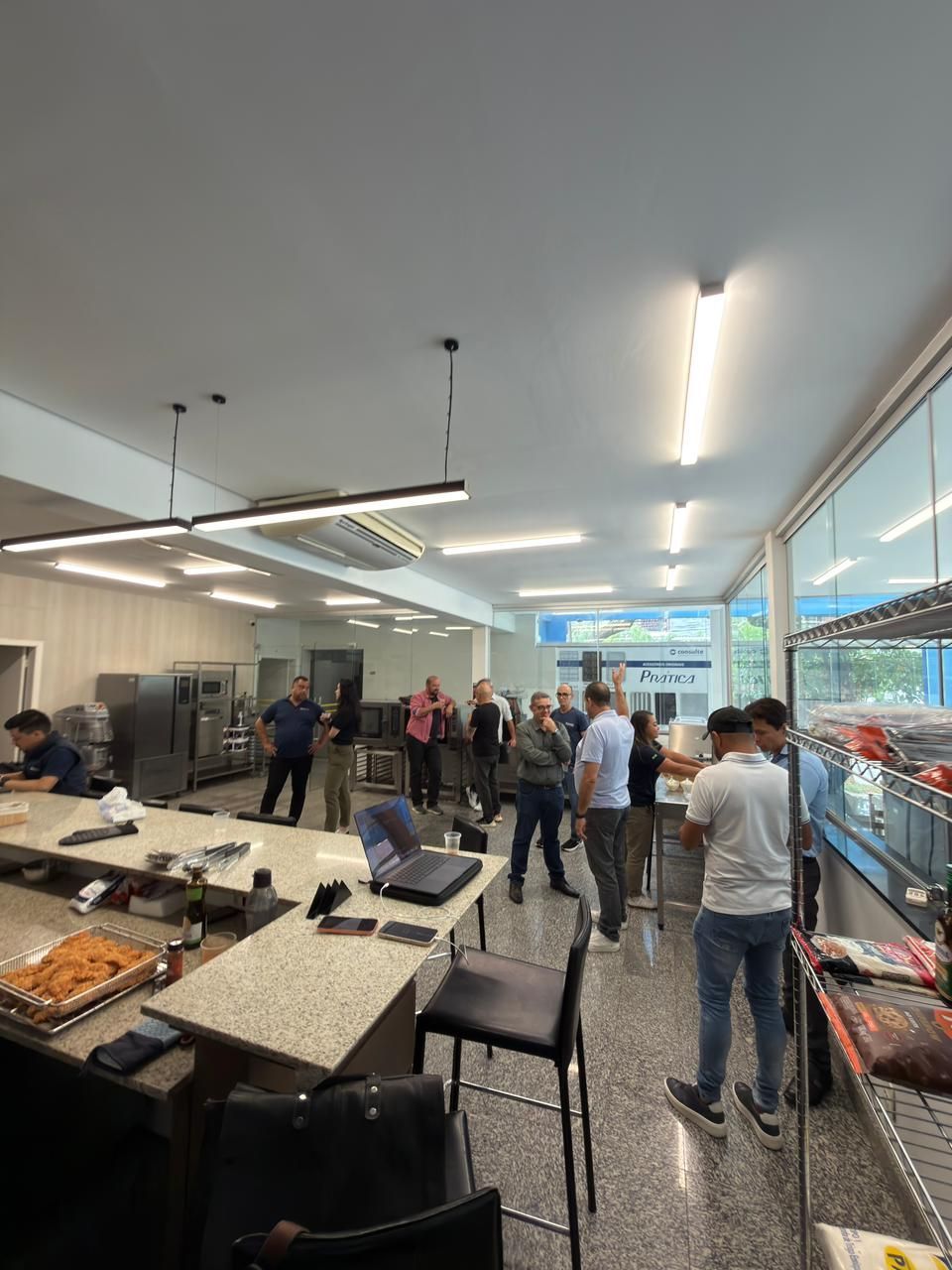 Grupo de pessoas em pé em uma cozinha comercial com janelas e eletrodomésticos.