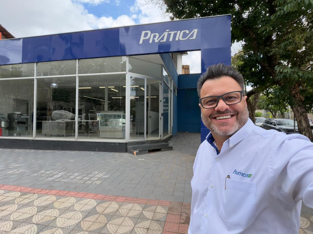 Homem sorrindo em frente a uma vitrine azul com a placa