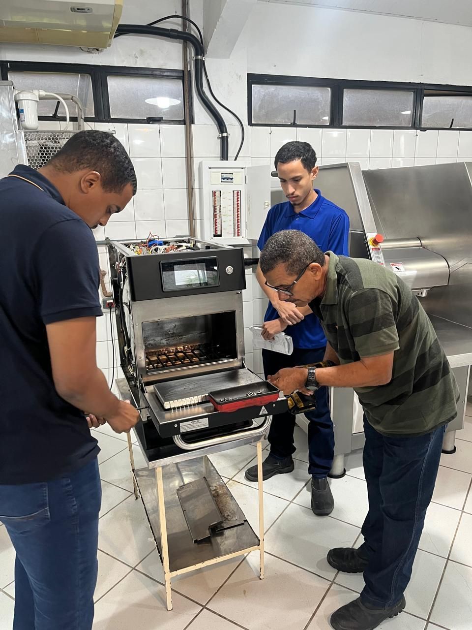 Três pessoas consertando um forno industrial em uma cozinha.